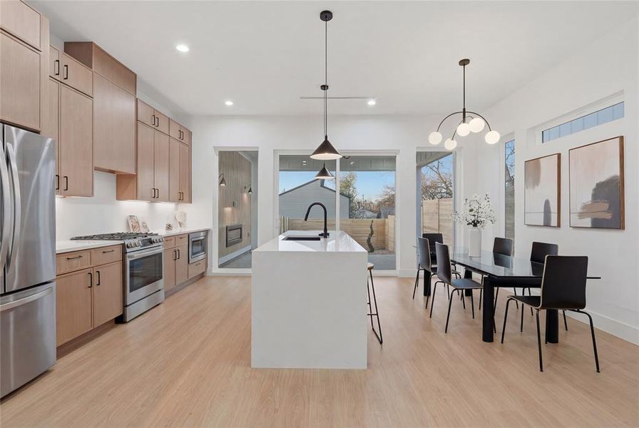 Kitchen with stainless steel appliances, an island with sink, light wood-style flooring, light stone countertops, and hanging lights