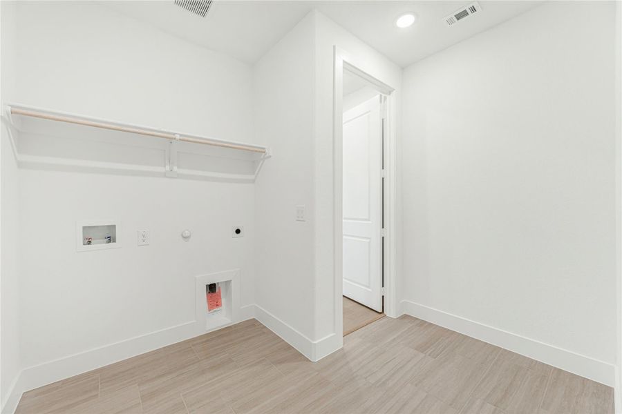 Laundry room with wall-mounted shelf, washer and dryer hookups, and light wood-look tile flooring Laundry room with wall-mounted shelf, washer and dryer hookups, and light wood-look tile flooring