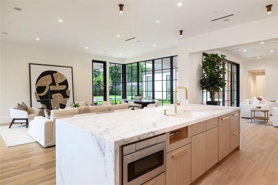 Kitchen with open floor plan, light brown cabinetry, light wood-type flooring, light stone countertops, and recessed lighting Kitchen with open floor plan, light brown cabinetry, light wood-type flooring, light stone countertops, and recessed lighting