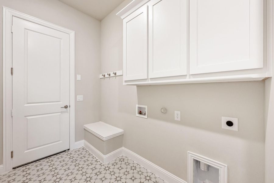 Laundry room with white upper cabinets, wall hooks, patterned tile floor, and washer and dryer hookups