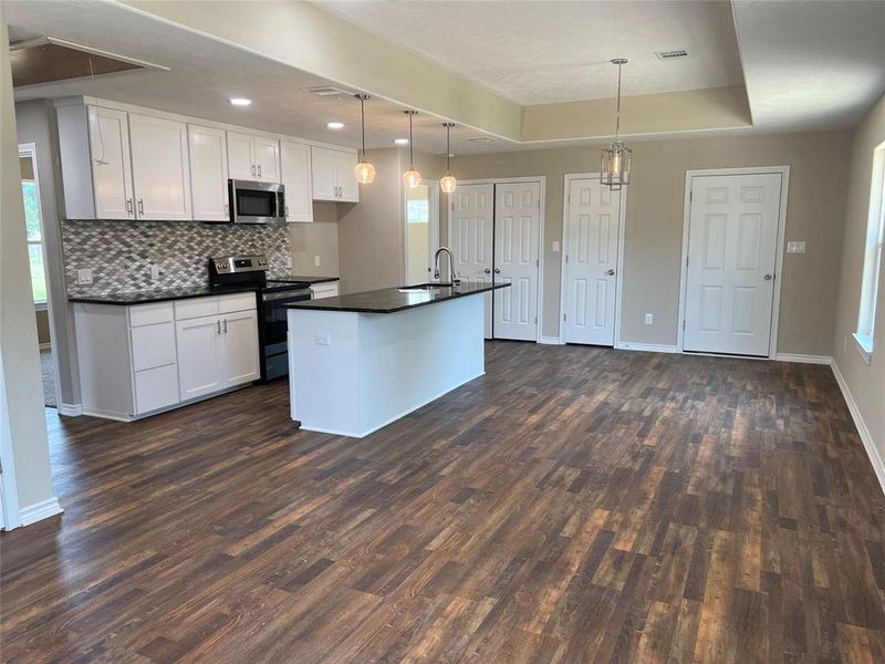Kitchen featuring pendant lighting, white cabinets, stainless steel appliances, a center island with sink, and tasteful backsplash