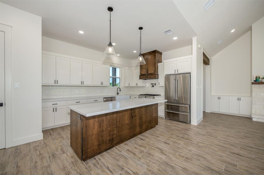 Kitchen with white cabinets, pendant lighting, a kitchen island, high end refrigerator, and decorative backsplash