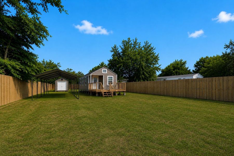 A spacious, green yard features a charming small home with an elevated deck, an open-sided carport (in process of installation), and a separate storage shed.