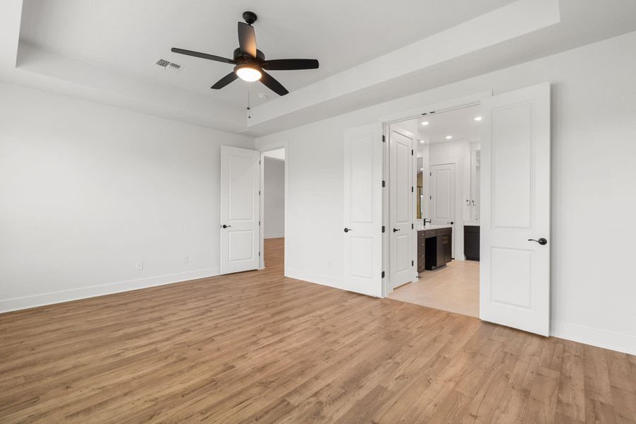 A well-proportioned bedroom with rich wood flooring, flowing into a private en-suite bathroom.