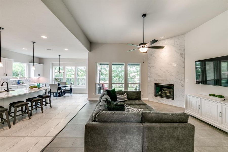 Living room with ceiling fan, high vaulted ceiling, sink, a high end fireplace, and light tile floors