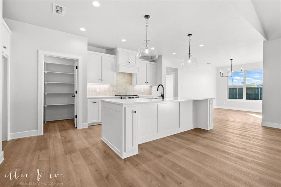 Kitchen featuring white cabinets, hanging light fixtures, tasteful backsplash, a kitchen island with sink, and recessed lighting