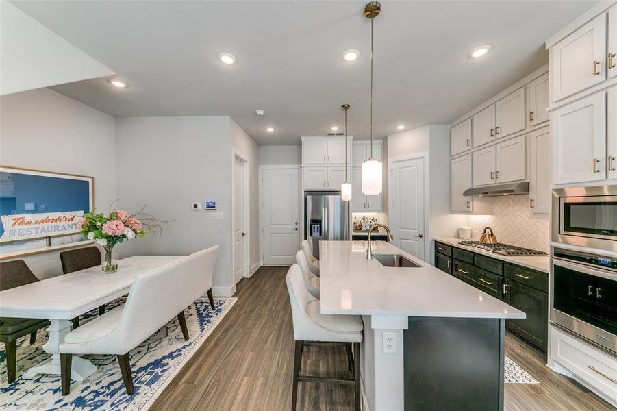 Kitchen with sink, hanging light fixtures, stainless steel appliances, an island with sink, and hardwood / wood-style flooring