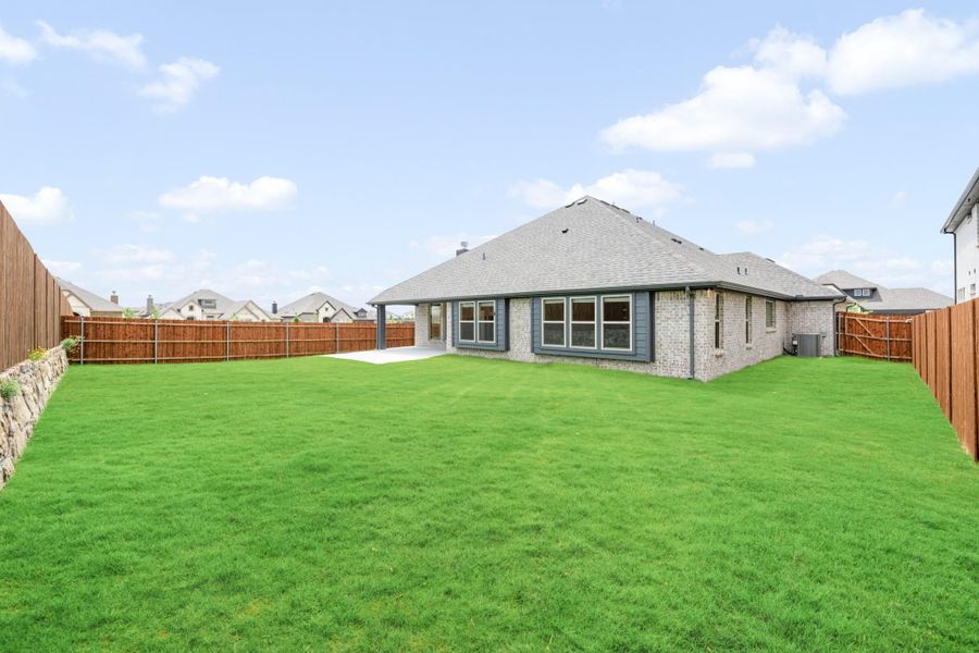 Brick home rear exterior with large grassy backyard, covered patio, and wood privacy fence Brick home rear exterior with large grassy backyard, covered patio, and wood privacy fence