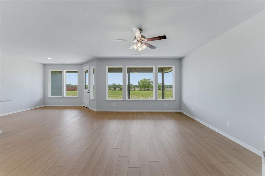 Expansive room featuring wood-finish flooring, light gray walls, and a ceiling fan with integrated lighting Expansive room featuring wood-finish flooring, light gray walls, and a ceiling fan with integrated lighting