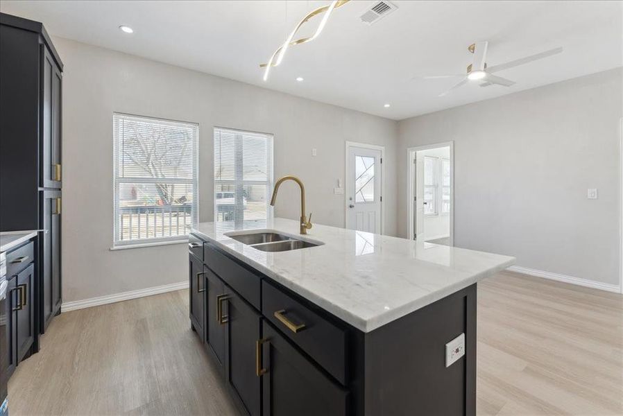 Kitchen with baseboards, a sink, a center island with sink, and light wood-style floors