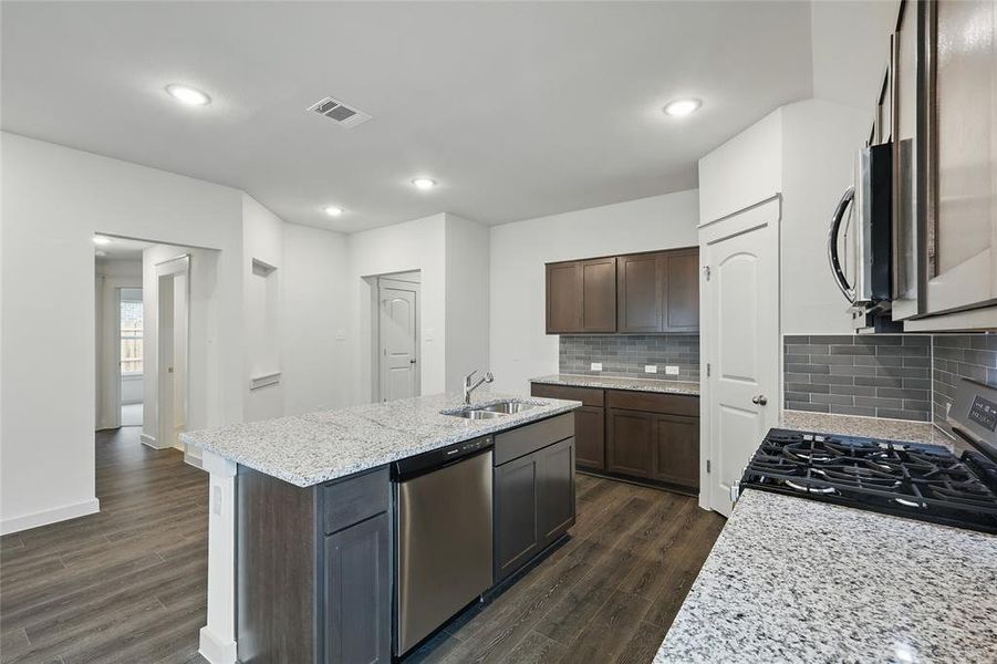 Kitchen with stainless steel appliances, light stone countertops, dark wood finish cabinets, backsplash, and dark wood-type flooring Kitchen with stainless steel appliances, light stone countertops, dark wood finish cabinets, backsplash, and dark wood-type flooring