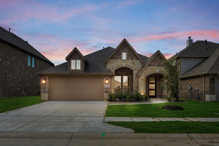 Single-story home with brick and stone exterior, two-car garage, arched entry, and green front lawn at dusk