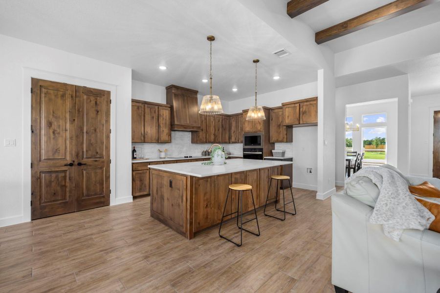 Kitchen with a kitchen breakfast bar, decorative light fixtures, beam ceiling, a spacious island, and light wood-type flooring