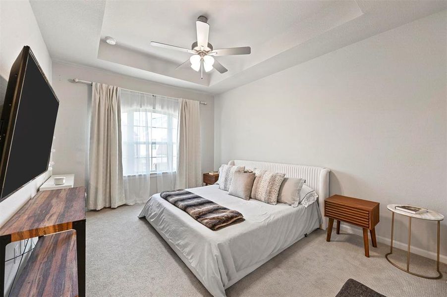 Carpeted bedroom featuring a raised ceiling and a ceiling fan Carpeted bedroom featuring a raised ceiling and a ceiling fan