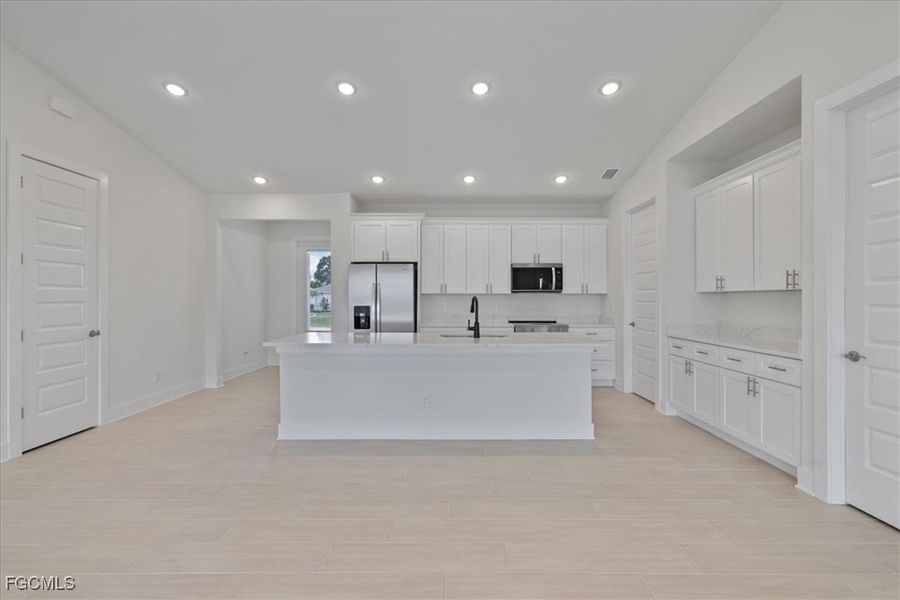 Kitchen with white cabinets, appliances with stainless steel finishes, recessed lighting, a kitchen island with sink, and light stone countertops
