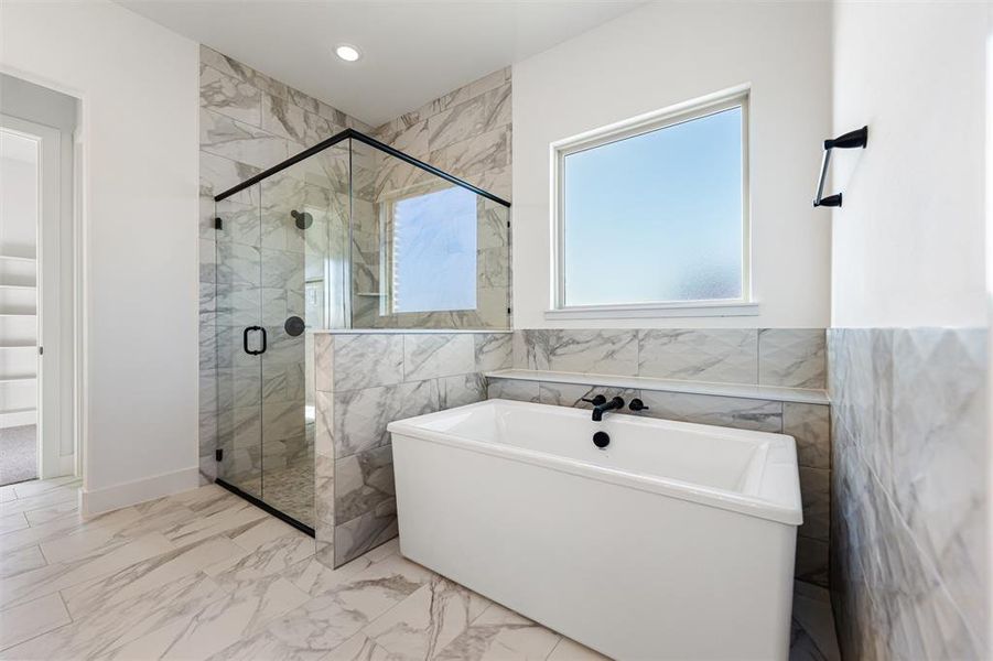 Bathroom with a soaking tub, light marble finish flooring, and a marble finish shower