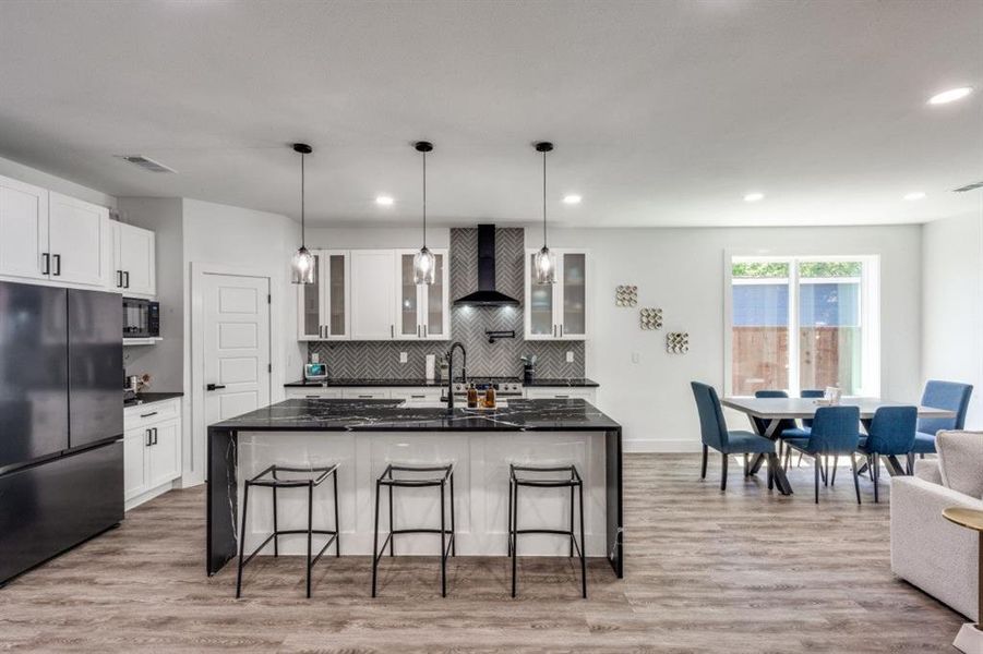 Kitchen featuring black appliances, wall chimney range hood, backsplash, a kitchen bar, and light wood-style floors