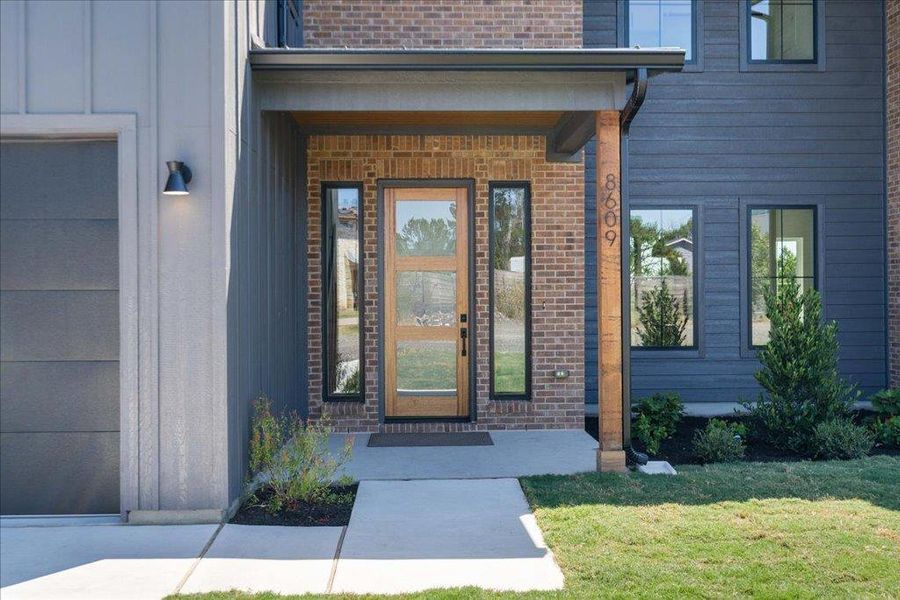 View of exterior entry featuring brick siding, a porch, a yard, and board and batten siding
