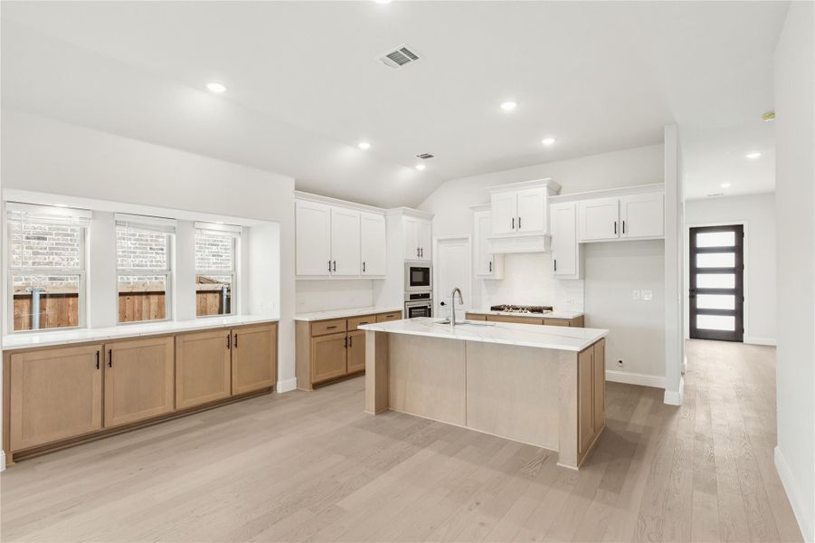 Kitchen with large center island, white upper cabinets, wood lower cabinets, and light hardwood floors