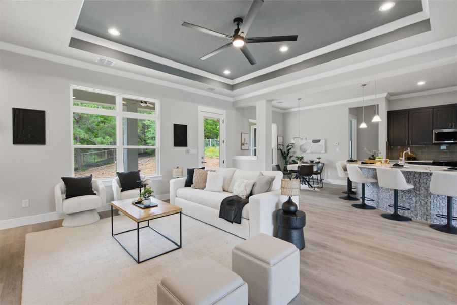 An open-concept living space with a tray ceiling and light wood-look flooring connects to a contemporary kitchen. An open-concept living space with a tray ceiling and light wood-look flooring connects to a contemporary kitchen.