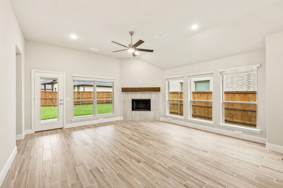 Open living room with tile fireplace, ceiling fan, wood-look floors, and large windows overlooking backyard Open living room with tile fireplace, ceiling fan, wood-look floors, and large windows overlooking backyard