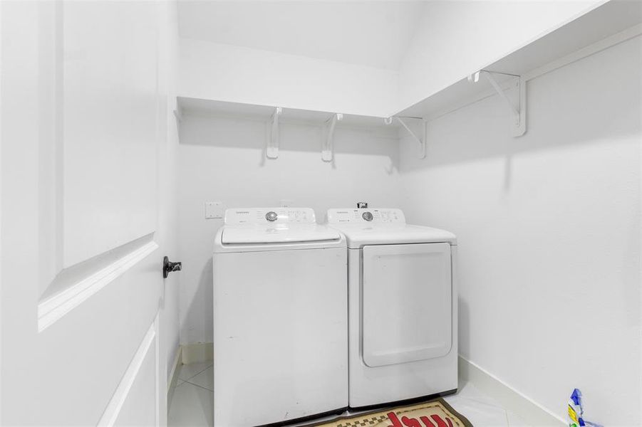 This photo shows a compact laundry room equipped with a washer and dryer. The space is bright with white walls and features a shelf above for additional storage.