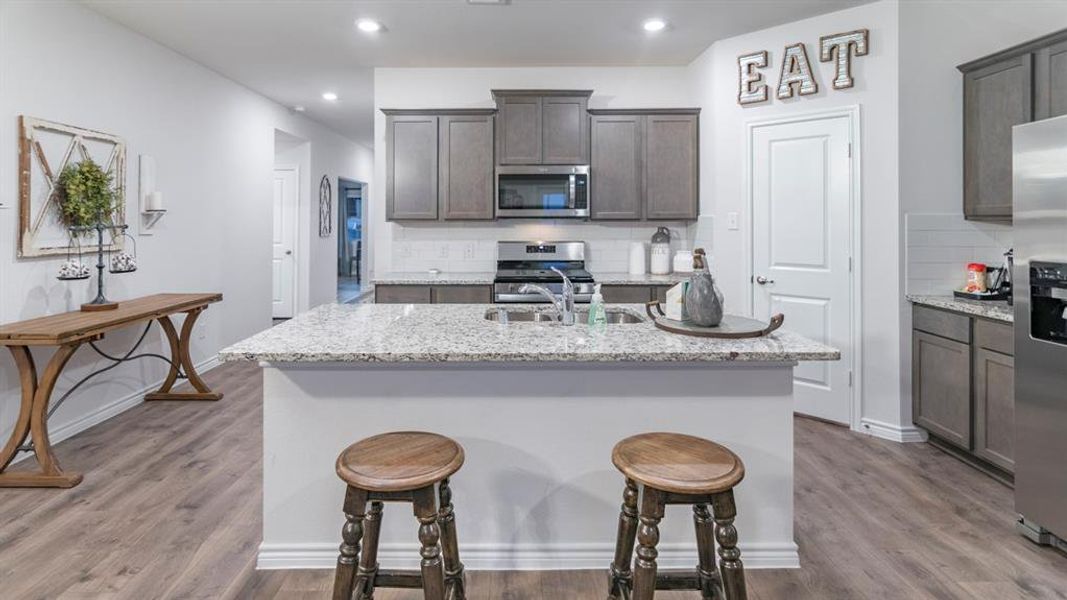 Kitchen featuring light stone countertops, a kitchen island with sink, stainless steel appliances, tasteful backsplash, and a kitchen breakfast bar Kitchen featuring light stone countertops, a kitchen island with sink, stainless steel appliances, tasteful backsplash, and a kitchen breakfast bar