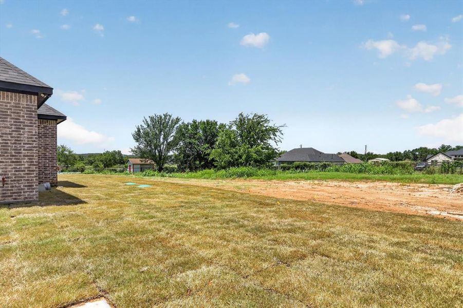 Expansive backyard with a large grassy area, brick exterior, dark shingle roof, and mature perimeter trees