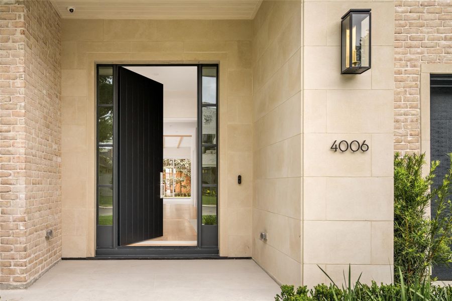 A limestone-clad entry with gas lantern sets a warm, elegant tone, complemented by manicured landscaping and sleek paver walkways leading to the front door.