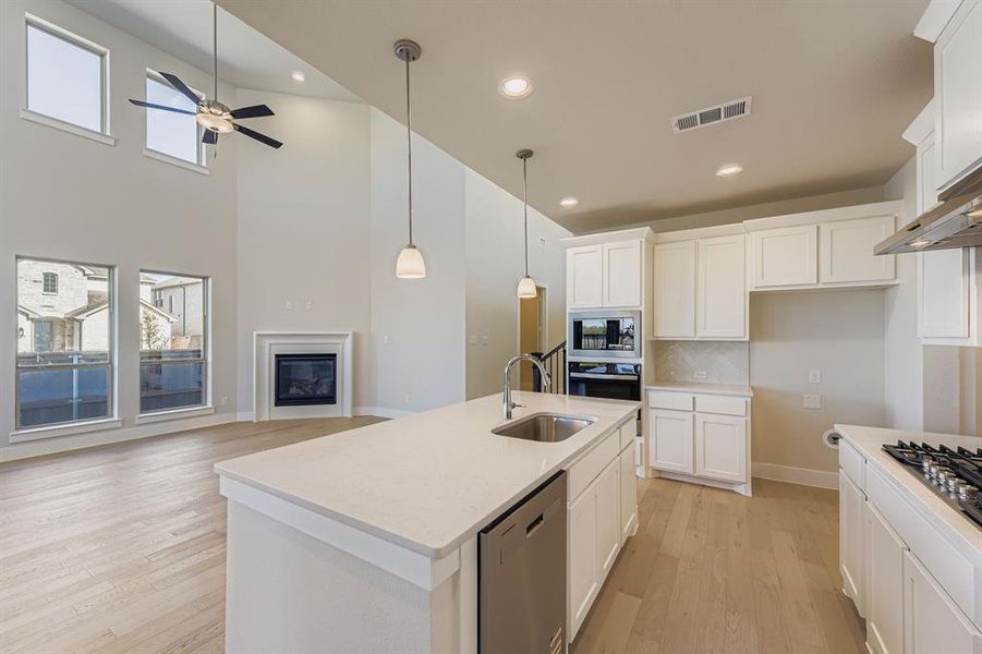 Kitchen featuring decorative backsplash, white cabinetry, light wood-style floors, decorative light fixtures, and stainless steel appliances