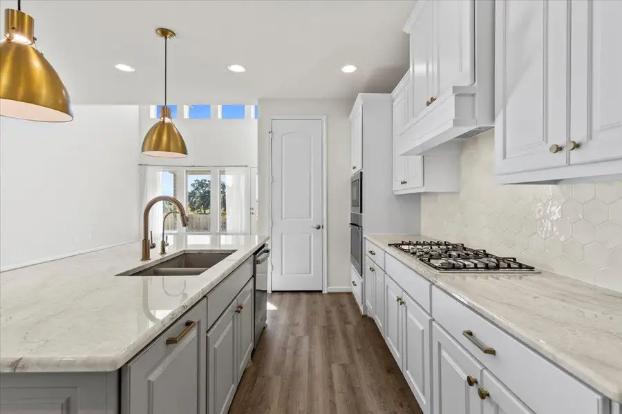 Kitchen with white cabinetry, light stone counters, an island with sink, recessed lighting, and pendant lighting Kitchen with white cabinetry, light stone counters, an island with sink, recessed lighting, and pendant lighting