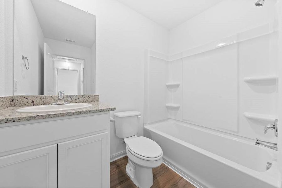 Secondary bathroom includes granite counters, designer white cabinetry and luxury vinyl plank flooring.