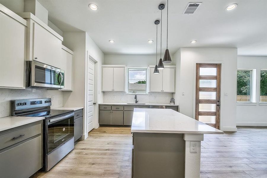 Kitchen with light hardwood / wood-style flooring, decorative light fixtures, stainless steel appliances, a kitchen island, and sink