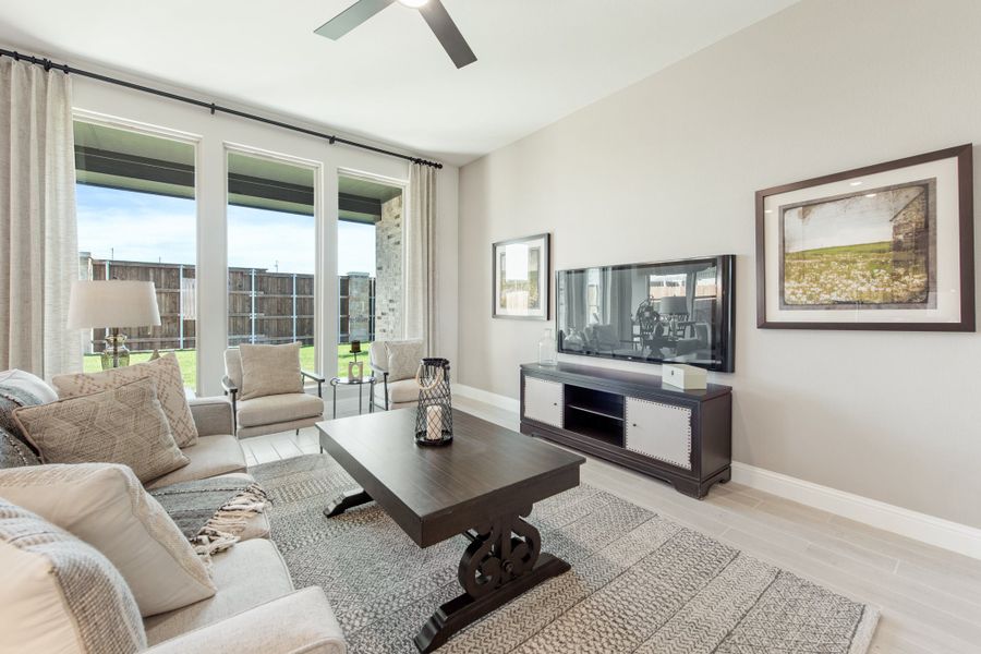 Living room with neutral sofas, dark wood coffee table, wall-mounted TV, and large windows with backyard view Living room with neutral sofas, dark wood coffee table, wall-mounted TV, and large windows with backyard view