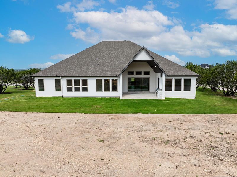 Rear view of property featuring a patio area, a shingled roof, and a yard