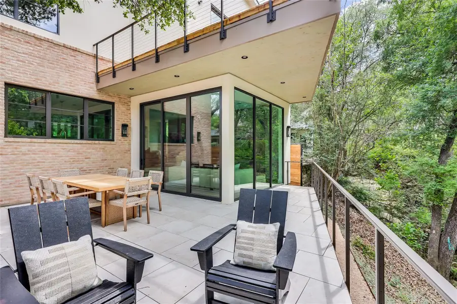 Spacious outdoor patio area featuring large format paver flooring, a brick exterior wall, and extensive glass sliding doors