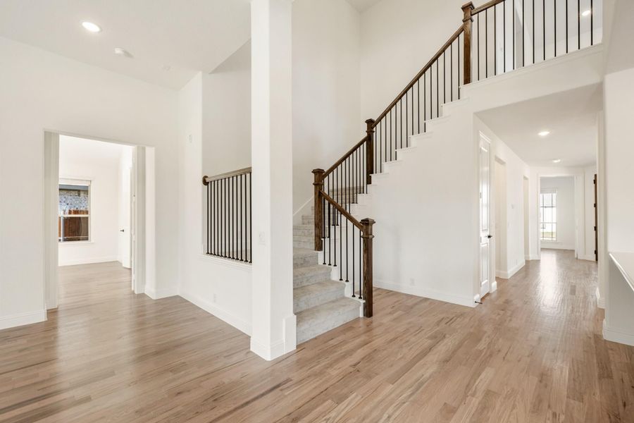 Open foyer with two-story staircase, wood and iron railing, and hardwood floors