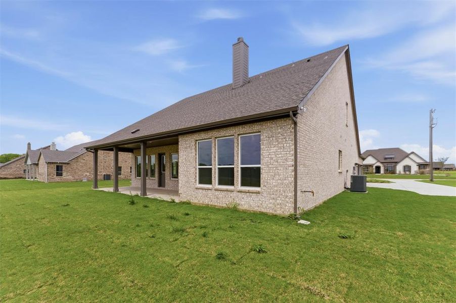 Back of house featuring a yard, brick siding, a chimney, and a patio