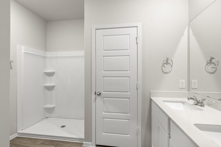 Image of a primary bathroom with light grey walls, a white jack and jill vanity, a large mirror and a white standing shower Image of a primary bathroom with light grey walls, a white jack and jill vanity, a large mirror and a white standing shower