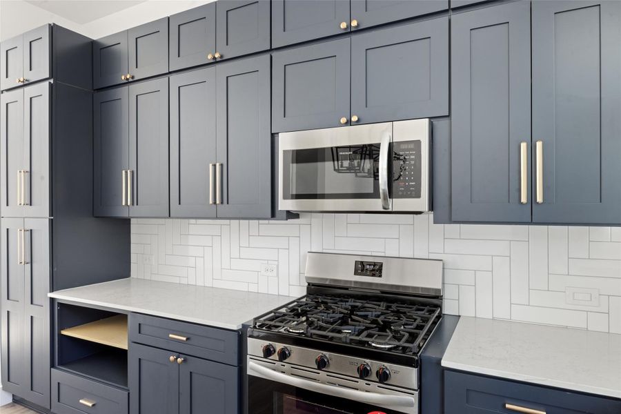 Kitchen featuring stainless steel appliances, light stone countertops, tasteful backsplash, and gray cabinets Kitchen featuring stainless steel appliances, light stone countertops, tasteful backsplash, and gray cabinets