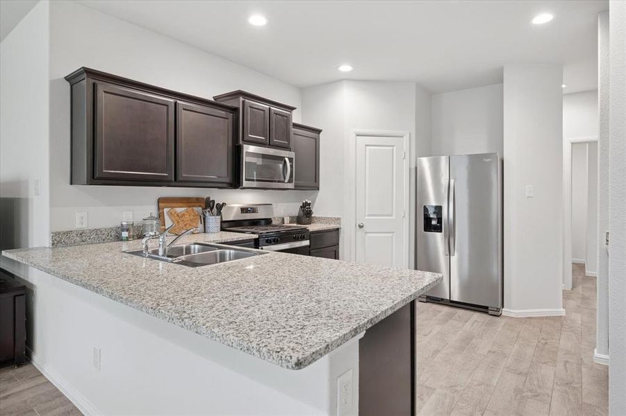 Kitchen featuring dark brown cabinets, appliances with stainless steel finishes, light wood-style flooring, a peninsula, and recessed lighting. Kitchen featuring dark brown cabinets, appliances with stainless steel finishes, light wood-style flooring, a peninsula, and recessed lighting.