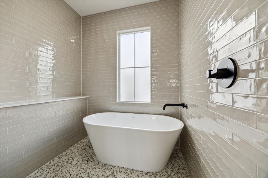 Experience luxury in the primary bathroom with a sleek freestanding tub, elegant tile walls, and a bright, airy ambiance.
