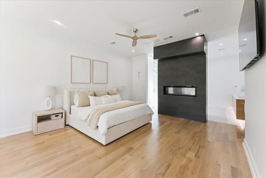 Bedroom with a large fireplace, light wood-style flooring, a ceiling fan, and recessed lighting
