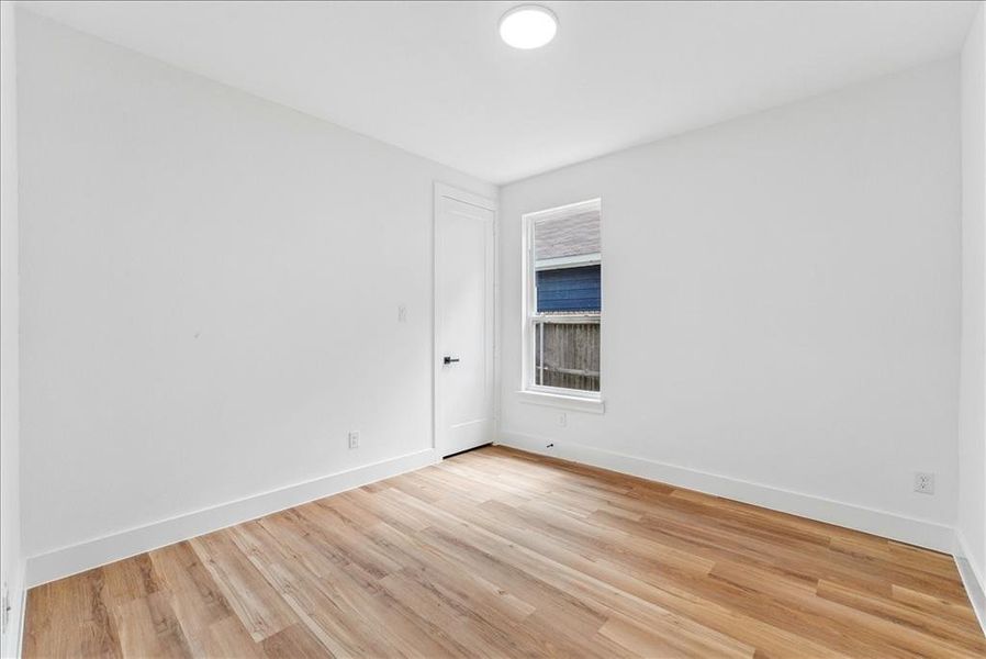 Bright room featuring wood-finish flooring, crisp white walls, a single window, and a flush-mount ceiling light fixture Bright room featuring wood-finish flooring, crisp white walls, a single window, and a flush-mount ceiling light fixture