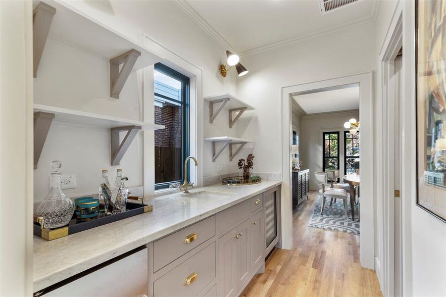 Bar with light stone countertops, sink, light hardwood / wood-style floors, and ornamental molding