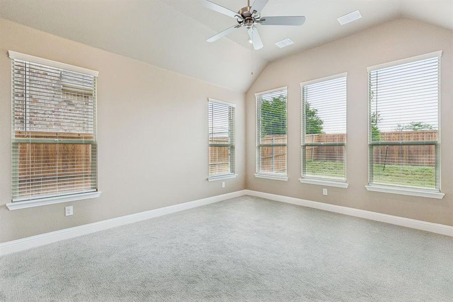 Carpeted spare room featuring vaulted ceiling and a ceiling fan