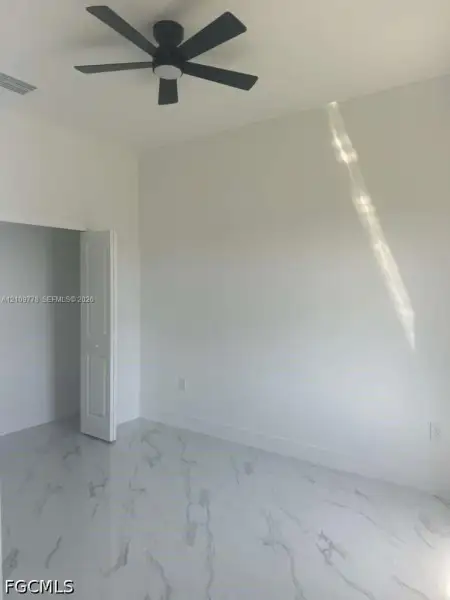 High-ceilinged room featuring large-format stone-finish tile flooring, matte black ceiling fan with integrated lighting, and a bi-fold door High-ceilinged room featuring large-format stone-finish tile flooring, matte black ceiling fan with integrated lighting, and a bi-fold door