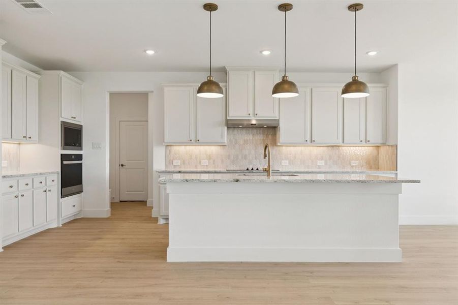 Kitchen with light stone countertops, white cabinets, light wood-type flooring, backsplash, and recessed lighting