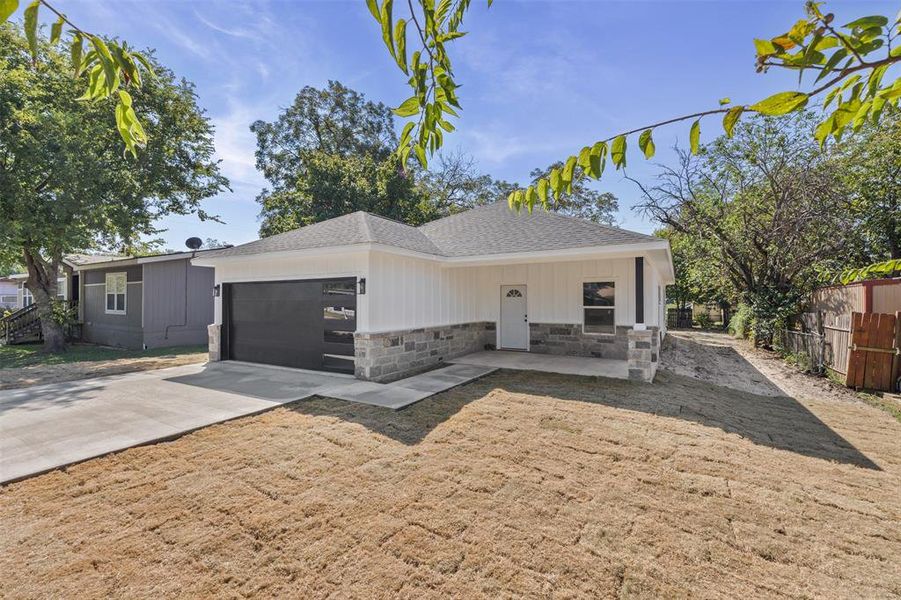 View of front of home with stone siding, roof with shingles, concrete driveway, and a garage
