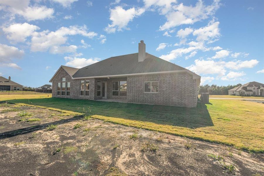 Back of house featuring brick siding, a lawn, a patio area, and a chimney